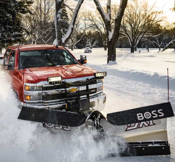 A red truck moving through heavy snow with BOSS Snowplows attached to its front
