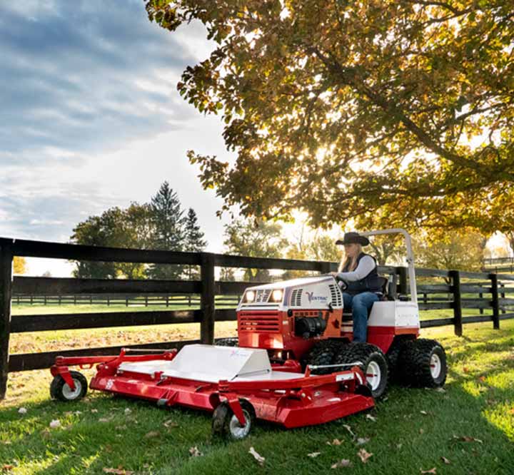 woman driving a commercial grade mower in a sun-filled pasture